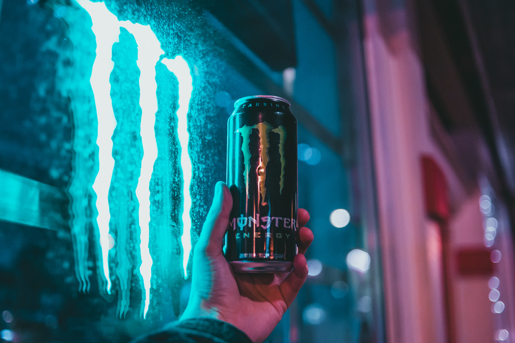 Hand Holding up Can of Energy Drink in front of Neon Sign